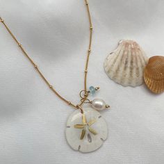 Legend has it that finding a sand dollar during a beach stroll is considered a lucky omen. So take a little bit of the beach and good luck with you wherever you go with our gorgeous Sand Dollar Charm Necklace. Features our most loved satellite chain, freshwater pearl, and blue zircon accents. Freshwater Baroque Pearl size: 6 to 8mm Blue Zircon roundel gemstone 4mm 14kt gold fill or sterling silver round beads 2mm 14kt gold fill or sterling silver satellite chain Real sand dollars are preserved a Sand Dollar Jewelry, Sand Dollar Necklace, Surf Jewelry, Diy Jewelry Display, Sand Dollars, Jewelry Accessories Ideas, Charm Necklace Silver, Gold Charm Necklace, Pearl Choker Necklace