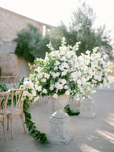 an outdoor ceremony with white flowers and greenery in vases on pedestals at the end