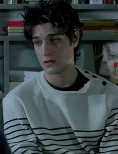 a young man sitting in front of a bookshelf