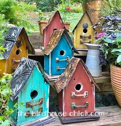 colorful birdhouses are lined up on a wooden bench in the garden with potted plants