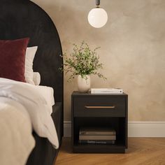 a nightstand with a plant on top of it next to a bed in a bedroom