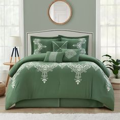 a bed with green comforter and pillows in a room next to a mirror on the wall