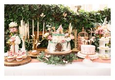 a table topped with cakes and cupcakes covered in frosting surrounded by greenery