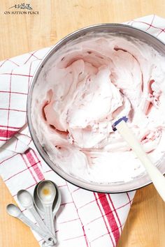 a metal bowl filled with whipped cream on top of a wooden table next to utensils