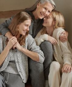 an older man and two younger women sitting on a couch smiling at each other with their arms around one another