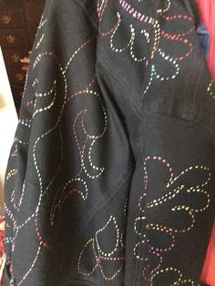 the back of a black jacket with multicolored circles on it and a pink shirt underneath