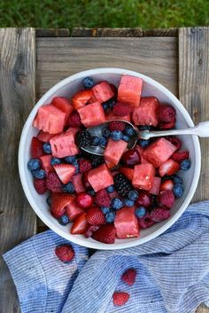 a bowl of watermelon, raspberries and blueberries with a spoon