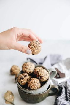 a hand holding a cookie ball over a bowl of oatmeal balls