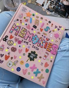 a pink book with lots of stickers on it sitting in someone's lap