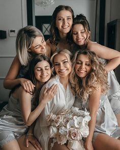 a group of bridesmaids hugging each other and posing for a photo in their wedding gowns