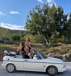 two women sitting on the roof of a white convertible car, one holding a child