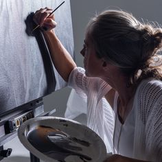 a woman is painting on the easel with a paintbrush and brush in her hand