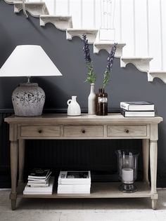 a table with a lamp, vases and books on it in front of stairs