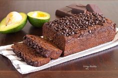 a loaf of chocolate cake sitting on top of a wooden table next to an avocado