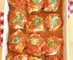 a casserole dish with tomato sauce and spinach garnished with basil leaves