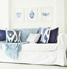 a white couch with blue and white pillows on it's back, in front of three framed pictures