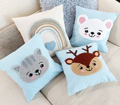 four pillows with animals on them sitting on a couch next to a stuffed bear and a rainbow