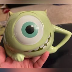 a hand holding a green monster mug with big eyes