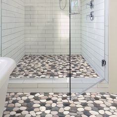 a walk in shower sitting next to a white bath tub under a window with rocks on the floor