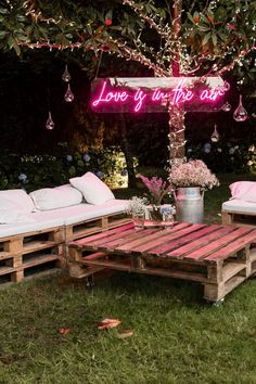 an outdoor seating area made out of pallets with pink lights and pillows on it