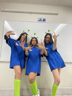 three girls in blue dresses and green socks posing for the camera with their hands up