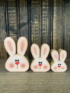 three small ceramic rabbits sitting next to each other on a wooden surface with wood planks in the background