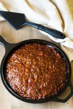 a skillet filled with chili sauce on top of a wooden table next to a spatula