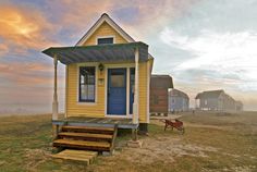 a small yellow house sitting on top of a grass covered field next to a red fire hydrant