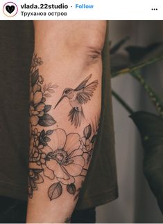 a person with a tattoo on their arm that has flowers and a bird flying over it