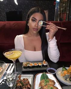 a woman eating sushi with chopsticks in front of her face at a restaurant