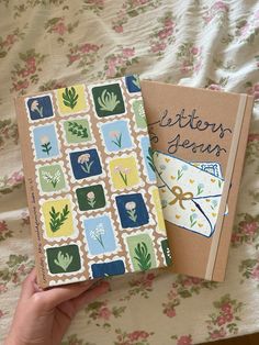 two notebooks sitting next to each other on top of a floral covered bed sheet