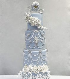 a three tiered blue wedding cake with white flowers and pearls on the top layer