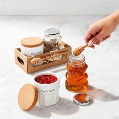 a person is holding a wooden spoon over some honey and jams on a counter