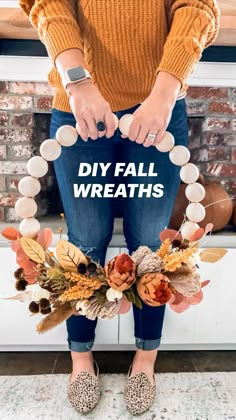 a woman standing in front of a fireplace holding onto a wreath made out of fake flowers