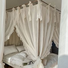 a canopy bed with white sheets and pillows