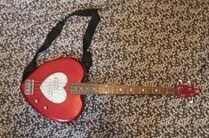 a red guitar laying on top of a bed next to a black bag with a white heart on it