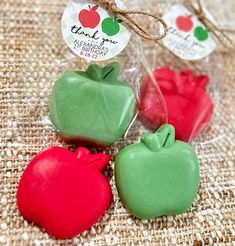 three apple shaped candies in plastic bags on a burlap surface with tags