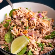 a bowl filled with shredded meat and garnished with cilantro, lime wedges