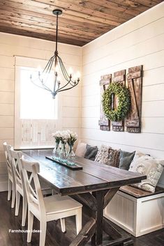 a dining room table with white chairs and benches in front of it, surrounded by wood plank ceilinging