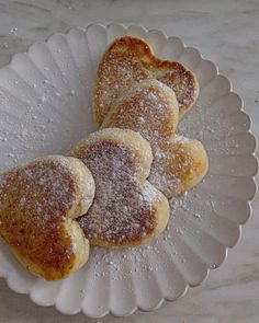 three heart shaped pastries on a white plate with sugar sprinkled over them