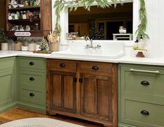 a kitchen decorated for christmas with green cabinets and white counter tops, greenery hanging over the sink