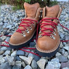 a pair of brown boots with red laces sitting on top of some rocks and gravel