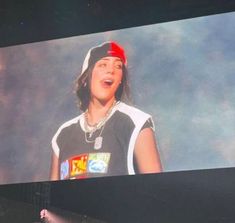 a person standing on a stage with a microphone in front of him and wearing a hat