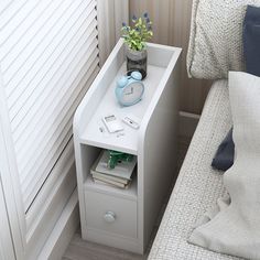 a nightstand with a clock and flowers on it next to a bed in a bedroom