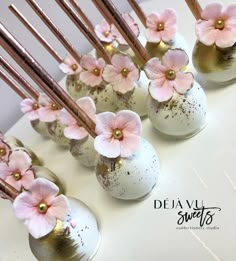 pink flowers are placed in white vases with gold sticks sticking out of the top