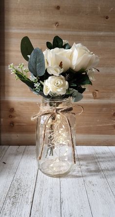 a glass jar filled with white flowers on top of a wooden table