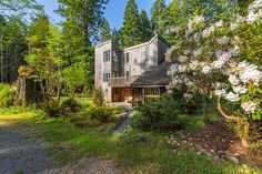 a house surrounded by trees and flowers in the woods with lots of greenery on either side