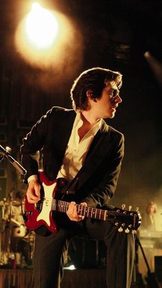 a man playing guitar while sitting on a stool in front of a microphone and stage lights