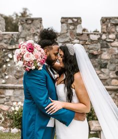 a bride and groom embracing each other in front of a stone wall at their wedding