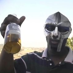 a man wearing a helmet and holding up a beer in front of his face with the sky behind him